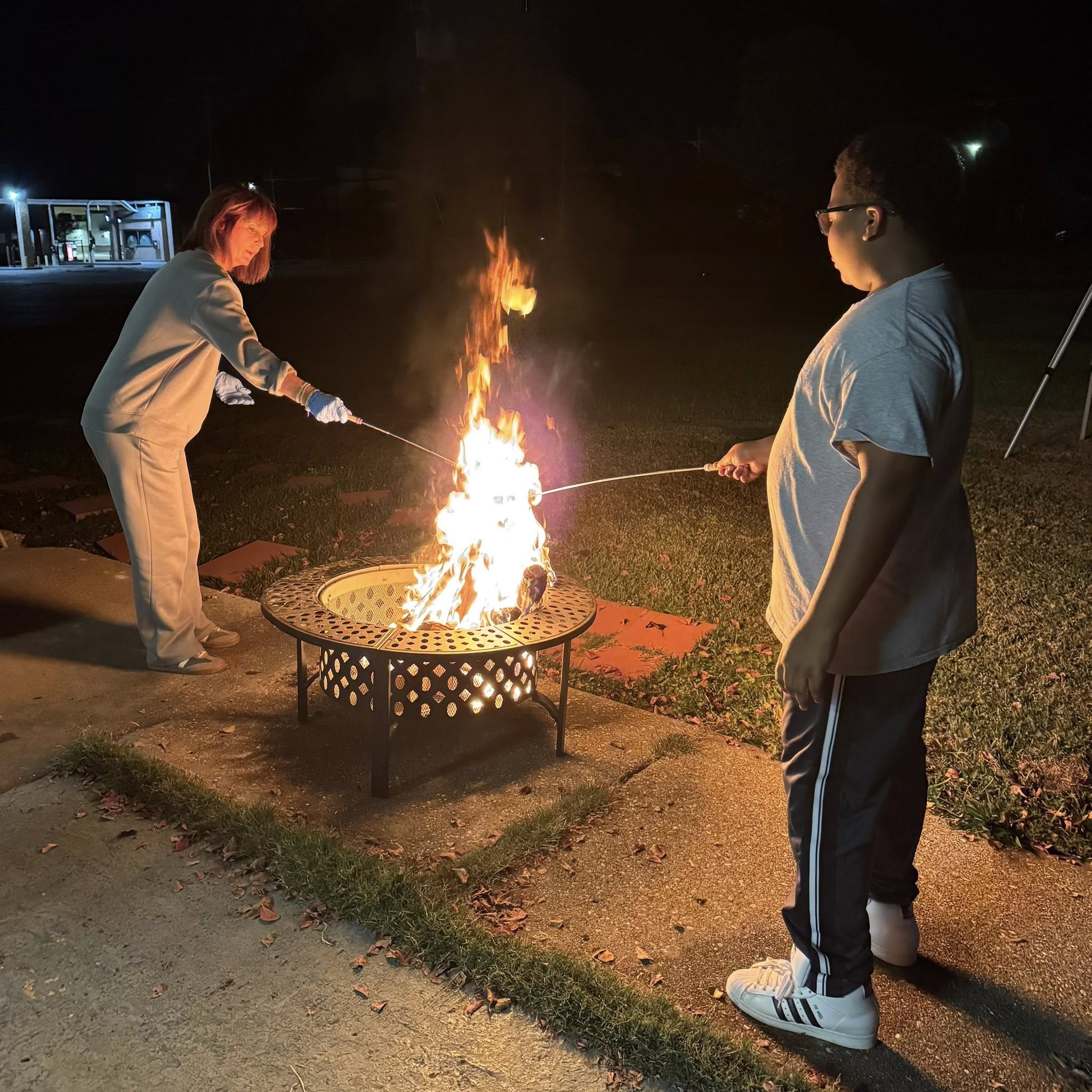 A woman and a boy roasting marshmallows over a firepit.